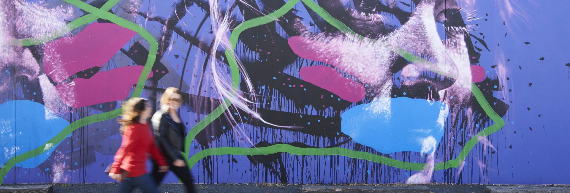 Two people walk past an outdoor street art mural in Bunbury
